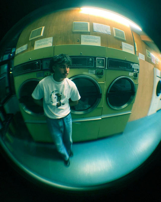 A person in a laundromat wearing a white t-shirt with unique artwork, standing next to vintage washing machines.