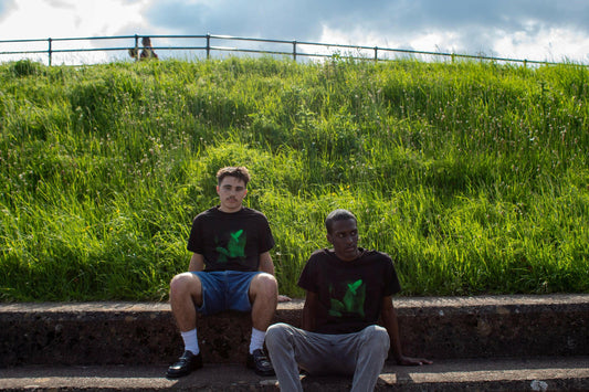 Two models wearing Sweet Spirit T-Shirts, screen printed design inspired by 'Les Yeux sans visage', sitting on a grassy hillside.