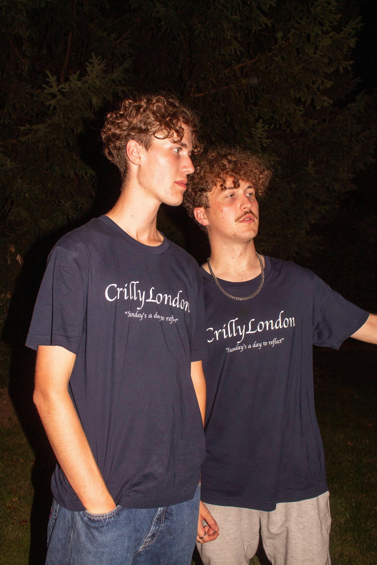 Two young men wearing limited edition Crilly London Billboard T-shirts in dark surroundings, celebrating reflection.